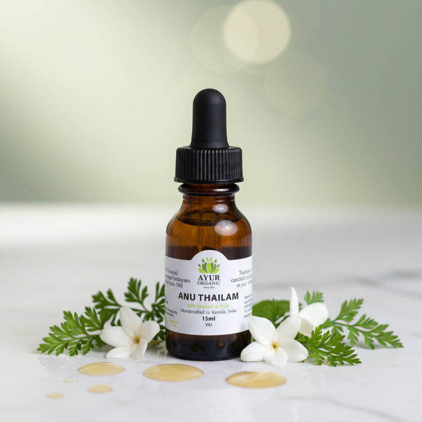 Bottle of Ayur Organic Anu Thailam with dropper surrounded by white flowers and green leaves on a light background