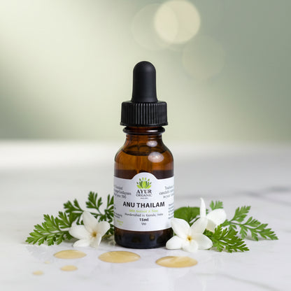 Bottle of Ayur Organic Anu Thailam with dropper surrounded by white flowers and green leaves on a light background