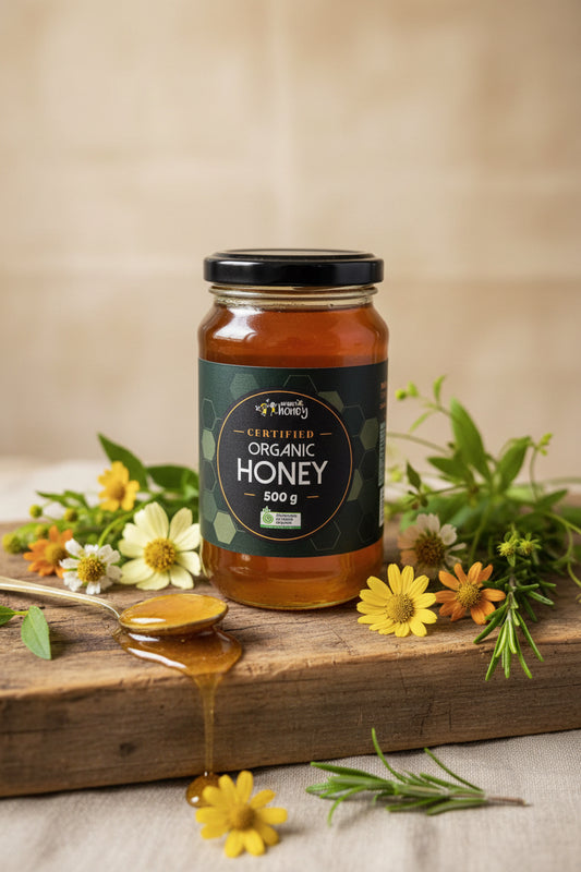 Jar of organic honey on a wooden board with flowers and a spoonful of honey.